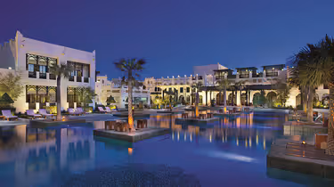 Hero/establishing shot of Sharq Village & Spa, a Ritz-Carlton Hotel, Doha, Qatar. A heritage Qatari village-style beach resort along the Doha coastline, with marbled Sheikh’s-palace design and a Michelin Key.
