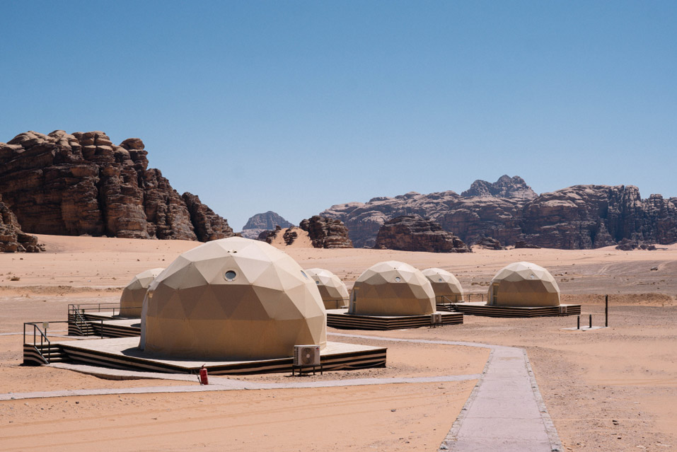 Hero/establishing shot of Sun City Camp, Wadi Rum, Jordan. A luxury desert glamping camp in Wadi Rum’s protected UNESCO desert — the originator of the Martian Dome, with transparent-roof bubble domes for in-bed stargazing alongside Bedouin-style and Royal tents.