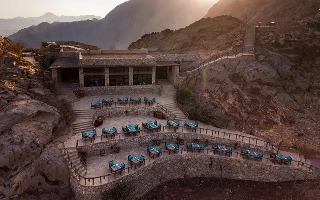 Hero/establishing shot of Six Senses Zighy Bay, Musandam, Oman (via Dubai). A paraglide-in barefoot-luxury all-villa hideaway styled as a traditional Omani fishing village, on a Musandam fjord bay reached via Dubai.