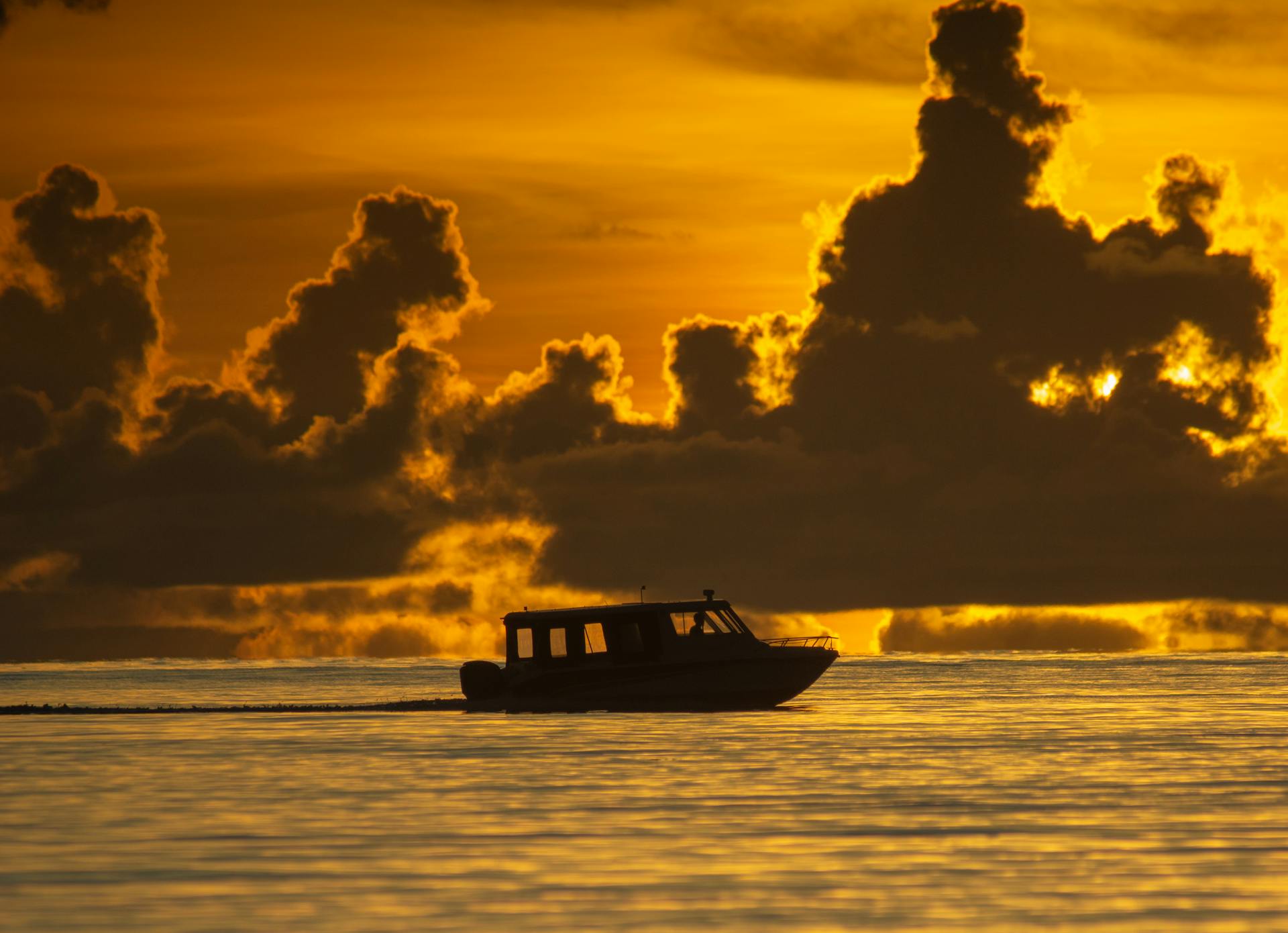 A catamaran out onto the lagoon as the light turns gold and pink behind Otemanu